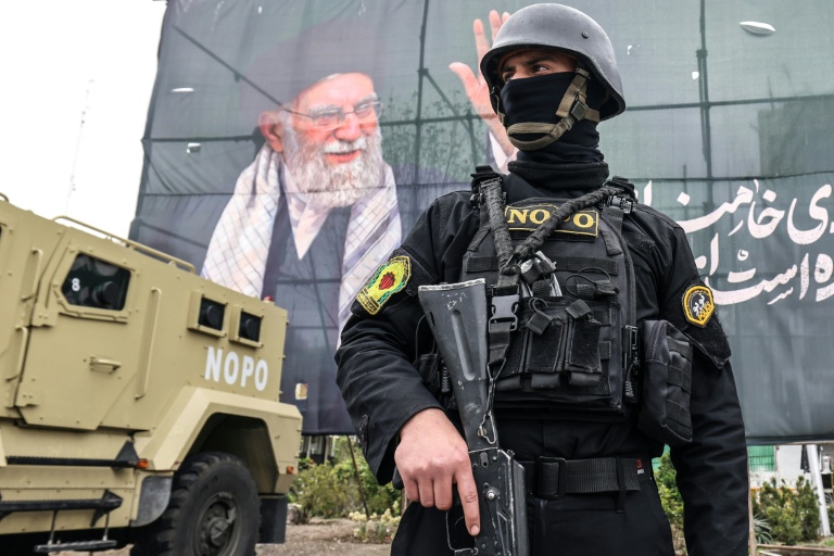 Photo for story: A member of the Iranian security forces stands guard next to a banner honouring Iran's slain supreme leader Ayatollah Ali Khamenei in Tehran