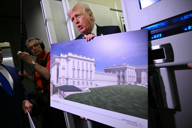 Photo for story: US President Donald Trump holds a rendering of the East Wing modernization as he speaks to reporters aboard Air Force One